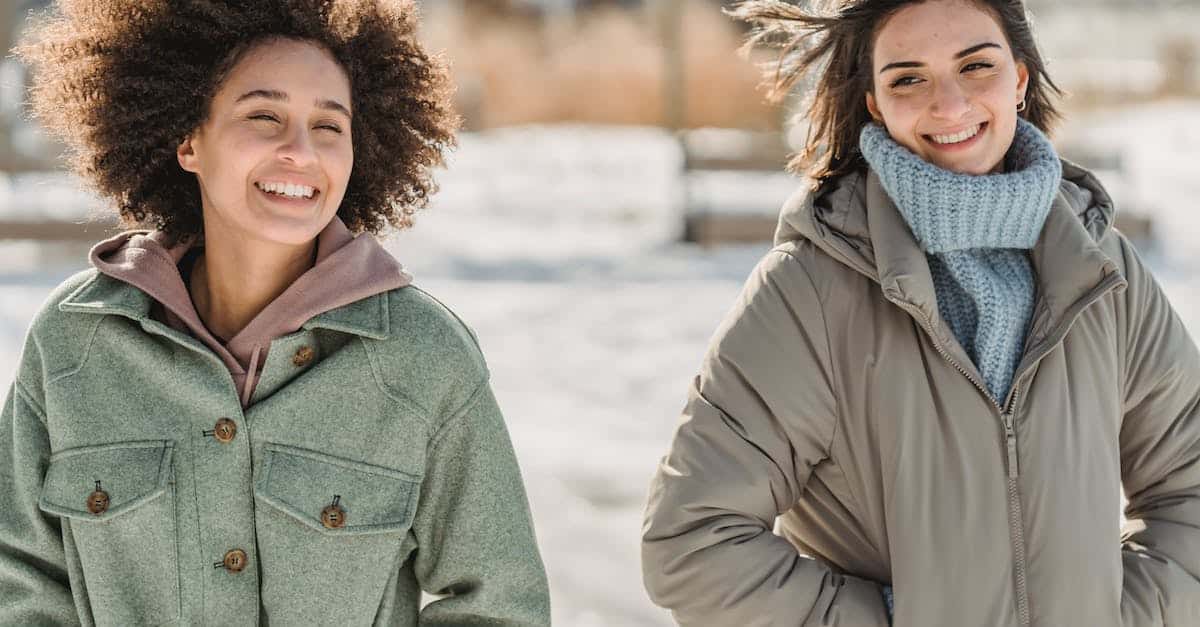 carefree-young-multiracial-female-friends-in-warm-wear-walking-together-with-hands-in-pockets-on-sno