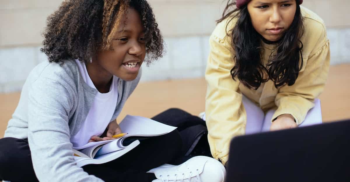 crop-attentive-diverse-schoolchildren-watching-laptop-while-studying-on-street-1