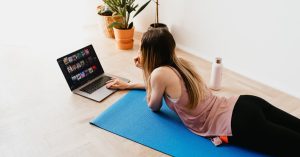 young-woman-lying-on-floor-on-mat-while-using-laptop-at-home
