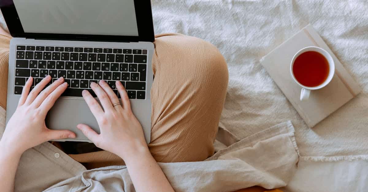 top-view-anonymous-remote-worker-typing-on-keyboard-of-laptop-with-blank-screen-while-sitting-with-c